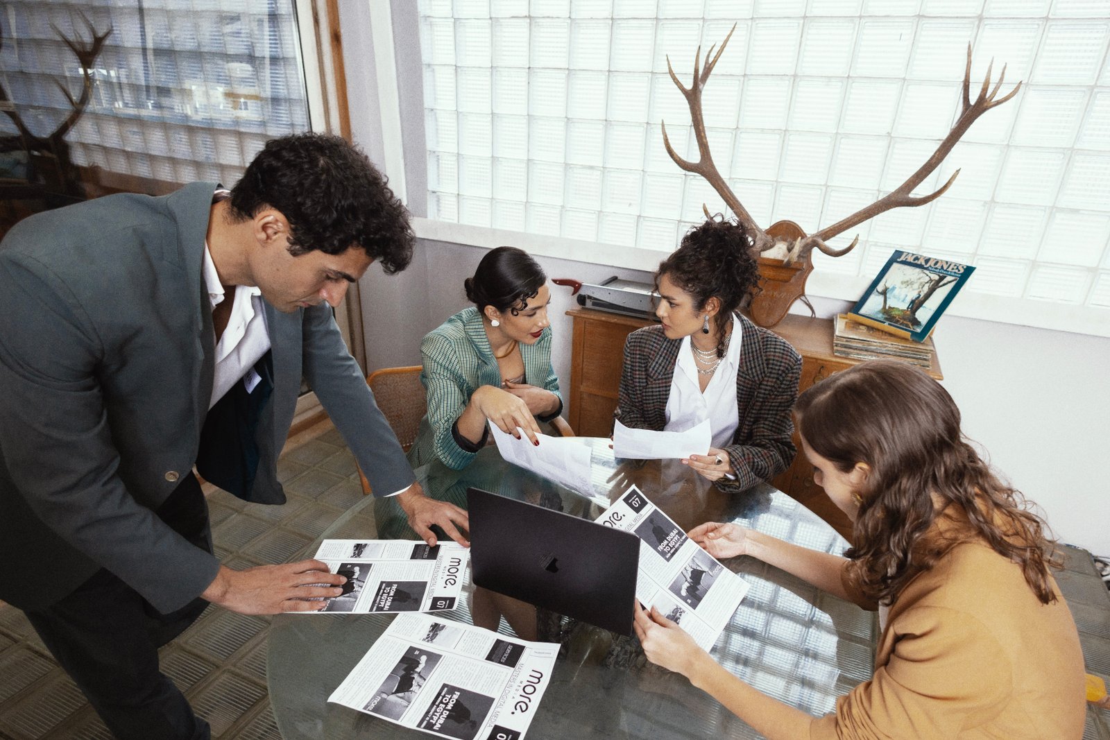 Office team collaborating on project with printed documents and laptop in modern workspace with antler decor